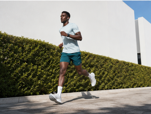 Läufer in türkisem Shirt joggt an einer grünen Hecke entlang – Laufplan 10 km